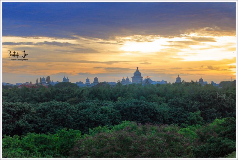 A view of sunset behind Vidhan Soudha in Bangalore with green trees in the foreground
